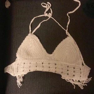 Vit virkad bikiniöverdel med knyt - Supersöt vit bikiniöverdel i virkad stil med knyt i nacken och ryggen. Triangelformade kupor och bredare band under bysten med fina virkade detaljer och fransar i kanterna. Perfekt för strandhäng eller festival.