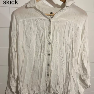 Vit skjorta med knappar - Vit skjorta med klassisk krage och knäppning framtill. Skjortan har lång ärm och är tillverkad i ett lätt och luftigt material som ger en avslappnad vibe. Perfekt för dig som gillar en clean och enkel stil.