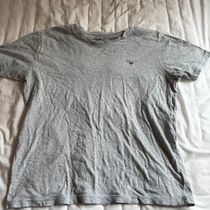 Grå Gant t-shirt  - Säljer min gråa T-shirt från gant. Gant loggan är tryckt på vänster sida. Säljer för att tröjan inte har använts på länge. Storlek 170 men passar en S.