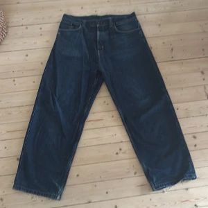 Wide jeans från Carhartt i mörk denim - Säljer ett par mörkblå jeans från Carhartt med bred passform och råa, fransiga benslut. Klassisk femficksmodell med Carhartt-logga på bakfickan. Jeansen är tillverkade i kraftig denim och har en riktigt loose och avslappnad vibe. Pros kan diskuteras