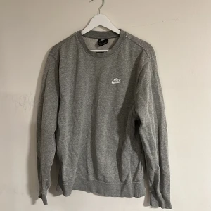 Tröja från Nike - En klassisk grå crewneck från Nike med vit logga broderad på bröstet. Tröjan har rund hals, långa ärmar och ribbade muddar. Tillverkad i mjuk bomullsmix som är perfekt för chill dagar eller till skolan. Storleken är S men funkar även till M. Finns lite färg på tröjan som syns på bild 3 och 4. Syns knappt men därav det nedsänkta priset. Skriv vid minsta fundering🌠🍾