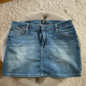 Blå jeanskjol från Lee - Snygg blå jeanskjol från Lee med klassiska fem fickor, bälteshällor och tydliga kontrastsömmar. Kjolen har dragkedja och knapp framtill med Lee-logga, samt läderpatch med Lee på baksidan. Perfekt för dig som gillar en chill och tidlös denimstil. LEE MINI SKIRT W 28. Ser ut precis som på bilderna🩵 #Fynd #Loppis #Vinted 