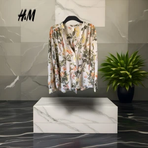 Blommig långärmad skjorta från H&M - Superfin blommig skjorta från H&M i vitt med gröna, gula och orange detaljer. Skjortan har knappar framtill, bröstficka och avslappnad passform. 