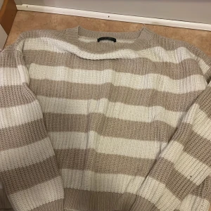 Randig stickad tröja i beige och vitt - Säljer en mysig stickad tröja med breda ränder i beige och vitt. Tröjan har en klassisk rund halsringning och långa ärmar. Perfekt för lager-på-lager och chill dagar. Ribbstickade muddar vid ärmslut och nederkant ger en snygg finish.