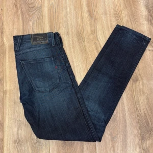 Replay Anbass mörkblå jeans, W30 L32 - Snygga mörkblå Replay Anbass jeans med klassisk femficksdesign och diskret Replay-logga på bakfickan. Jeansen har en slim passform och är tillverkade i mjukt bomullsdenim med lite stretch för extra komfort. Perfekta för dig som gillar stilrena och moderna jeans.