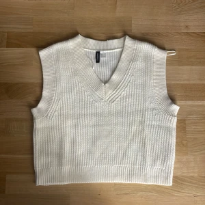 Vit stickad väst från H&M Divided - Snygg vit stickad väst från H&M Divided i storlek S. Västen har v-ringning och ribbade kanter, perfekt att styla över en skjorta eller t-shirt för en trendig lager-på-lager-look.