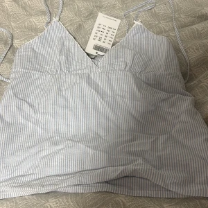 Randig linnetopp från Brandy Melville - Aldrig använt ,köpt 14 september,Supersöt linnetopp från Brandy Melville med smala blå och vita ränder. Toppen har tunna axelband, v-ringning och är ärmlös. Perfekt för varma dagar och enkel att matcha med jeans eller kjol. Tillverkad i mjuk bomull för en skön känsla.
