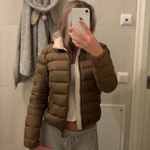 Brun Colmar pufferjacka med huva - Säljer en brun pufferjacka från Colmar med beige insida och huva. Jackan har quiltad design, dragkedja framtill och Colmar-logga på ärmen. Perfekt för kyliga dagar och riktigt snygg till streetwear-stil.