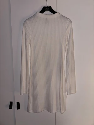 Vit ribbad långärmad klänning - Säljer en vit, ribbad klänning med lång ärm och enkel design. Klänningen har en rak passform och är tillverkad i mjukt material som sitter skönt mot kroppen. Perfekt för dig som gillar minimalistisk stil och vill ha något som är lätt att matcha.