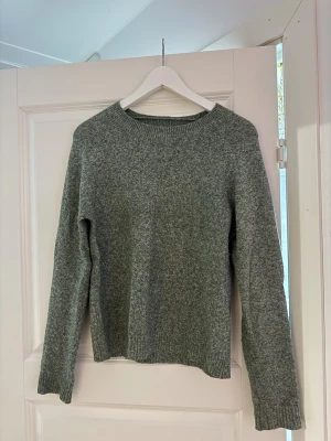 Grön stickad tröja från Vero Moda - Mysig stickad tröja från Vero Moda, grågrön melerad färg. Storlek S, normal passform och rund halsringning. Perfekt till både jeans och tights när du vill vara varm men ändå se lite stylish ut.  Sökord: Vero Moda, stickad tröja, grön tröja, grågrön, sweater, kofta, pullover, storlek S, höst, vinter, mysig, basic, vardagsplagg