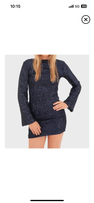 Mörkblå glittrig paljettklänning - Supersnygg mörkblå kort paljettklänning med lång ärm och rak passform. Klänningen har en hög hals och är täckt av glittrande paljetter som verkligen fångar ljuset. Perfekt för dig som vill sticka ut på festen eller nyår. Materialet känns mjukt och följsamt.