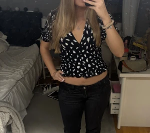 Svart blus med vit mönster - Säljer en svart blus med vita detaljer och djup v-ringning. Toppen har korta puffärmar, tajt midja och volangkant nedtill. Den är i storlek M egentligen men tycker passformen är mer som S!! Hör av er om ni har frågor!
