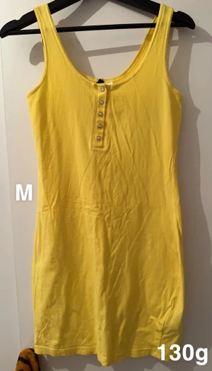 Gul ärmlös kortklänning med knappar - Snygg gul kortklänning i bomull med rund hals och knappar framtill. Klänningen är ärmlös och har en enkel, figurnära passform som känns både fräsch och bekväm. Perfekt för varma dagar och enkel att styla med sneakers eller sandaler.🌸 Fint använt skick. Storlek m
