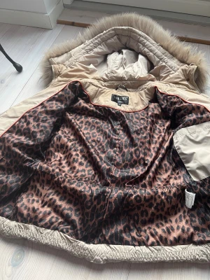 Vinter jacka - Snygg beige pufferjacka från Hollies med äkta päls runt luvan i nyskick. Jaxkan är som ny och har inga skavanker utom lite missfärgning runt nacken med det är inget som märks. Passar perfäkt till vintern. Skriv privat för frågor🫶