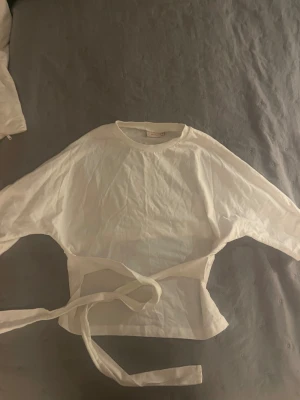 Knyttopp från Nelly - Säljer en vit knyt topp från Nelly i storlek Xs som är använd ungefär 3 ggr och i ett väldigt bra skick!! Toppen har långa ärmar och knytband i midjan som ger en snygg passform. Tillverkad i mjuk bomull och passar perfekt till jeans eller kjol.