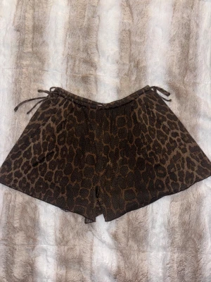 Leopardmönstrade shorts från H&M XS - Säljer ett par bruna leopardmönstrade shorts från H&M i storlek XS. De har snörning i midjan och är tillverkade i ett mjukt, stretchigt material. Perfekta för dig som vill sticka ut med ett djurmönster och gillar bekväma plagg.