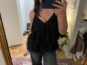 Svart volangig linnetopp från Zara - Svart linnetopp från Zara med flera lager volanger och tunna axelband. 