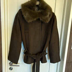 Mörkgrön kappa med fuskpäls från Zara - Så fin ullkappa från Zara med bred krage i fuskpäls och knytskärp i midjan. Jackan har lång ärm, två fickor fram och en asnajs lite loose passform. Perfekt för dig som vill ha en stilren och mysig look under höst och vinter. Helt ny, alla lappar kvar, slutsåld på hemsidan 🫶