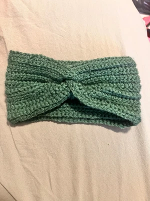 Grön virkad pannband twistad - Mysigt grönt pannband i virkat garn med twistad knut framtill. Perfekt för att hålla öronen varma och ge en chill vibe till din outfit. Mjuk och stretchig, passar de flesta huvudstorlekar. Handgjord!