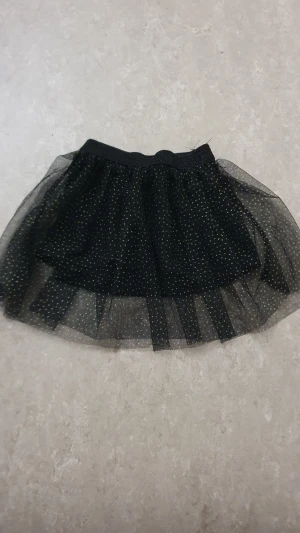 Kjol - Supersöt svart kjol från mywearbaby med glittriga guldprickar och ett lager av tunn tyll. Kjolen har ett mjukt resårband i midjan och är fodrad med svart tyg för extra komfort. Perfekt för dig som gillar lite extra glitter i vardagen.