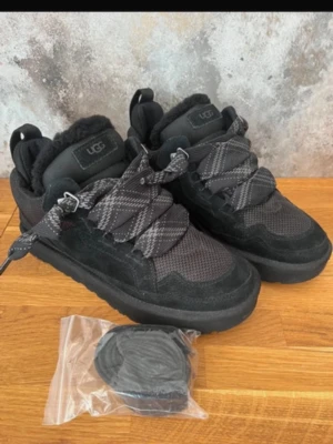 Svarta sneakers från UGG med foder - Snygga svarta sneakers från UGG med breda, mönstrade snören och mysigt foder. Ovandelen är i mocka och mesh, vilket ger både stil och komfort. Skorna har platt sula och rund tå, perfekta för kalla dagar. Extra skosnören medföljer.