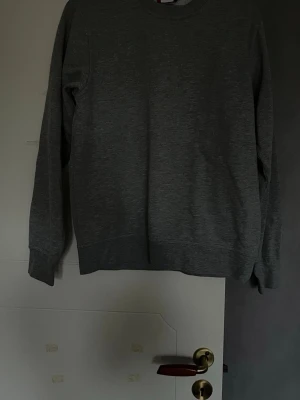 Grå sweatshirt från Clique, storlek S - En enkel och stilren grå sweatshirt från Clique i storlek S. Tröjan har rund hals, långa ärmar och ribbade muddar vid ärmslut och nederkant. Perfekt för chill dagar eller när du vill ha en basic look. Materialet är mjukt och skönt, troligen bomull och polyester.