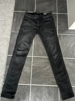 Replay Anbass svarta slim jeans - Svarta Replay Anbass jeans med slim fit och klassisk femficksdesign. Jeansen har snygga detaljerade sömmar, med Replay-logga på bakfickan och läderpatch i midjan. Materialet är stretchigt jeans för skön passform. Jag skulle säga att dem är 7/10 i skick, har använt dem hyfsat mycket men dem ser fortfarande väldigt bra ut.