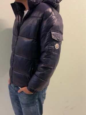 Mörkblå pufferjacka från Moncler - Säljer en mörkblå pufferjacka från Moncler med glansig finish och huva. Har använt den 5-6 gånger priset går att diskutera hör av dig om du har några frågor!