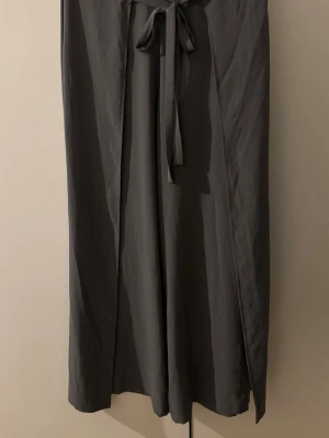 Grå wide byxor från Zara med knyt - Säljer ett par gråa wide byxor från Zara i storlek M. Byxorna har ett snyggt knytband i midjan och är tillverkade i ett mjukt och lätt material som ger en skön känsla. Passar perfekt om du gillar en avslappnad och stilren look.