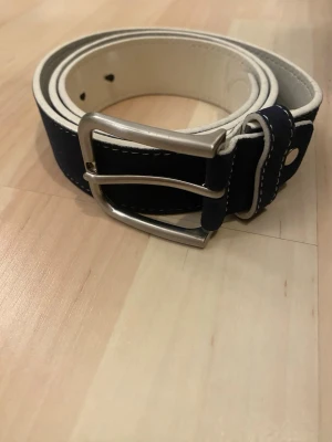 bälte från ovs, italien - Bilderna visar ett bälte från OVS i storlek 90/95. Bältet är mörkblått med vit insida och har ett metallspänne.