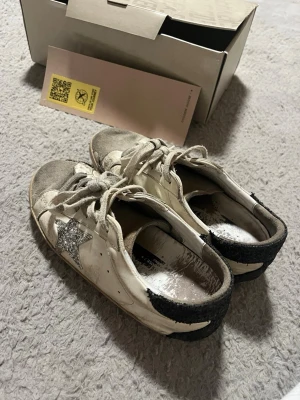 Golden Goose vita sneakers med glitterstjärna - Säljer dessa golden goose då dem inte längre används. De har slitage ja, men de går absolut fortfarande att använda., därav priset.