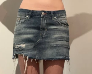 Blå jeanskjol med slitningar - Säljer en kort jeanskjol i blå denim med slitna detaljer och fransig nederkant. Midjemått rakt över 39 cm Längd: 30 cm