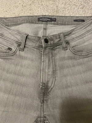 Jeans från Dressmann - Snygga grå jeans från Dressmann i slim fit-modell. Klassisk femficksdesign med knapp och dragkedja i midjan. Jeansen har en stilren look och är tillverkade i ett mjukt bomullsmaterial med lite stretch för extra komfort.