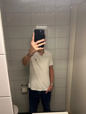 Vit pikétröja Polo Ralph Lauren - Säljer en klassisk vit pikétröja från Polo Ralph Lauren i slim fit. Tröjan har korta ärmar, krage med två knappar och den ikoniska broderade loggan på bröstet. Materialet är 100% bomull och passar perfekt till jeans eller shorts. Storlek är mellan xxs/xs. Två mindre nästan osynliga deffekter på framsidan som jag inte märkt av förrän nu. Skick 7/10 Hör av er vid minsta fundering!