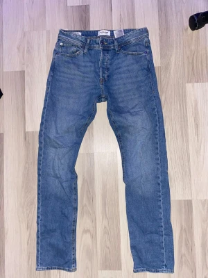 Blå tapered jeans från Jack & Jones - Säljer ett par blå jeans från Jack & Jones med tapered passform. Klassisk femficksdesign, normal midja och raka ben. Jeansen har snygga kontrastsömmar och är tillverkade i slitstarkt bomullsmaterial. Perfekt för dig som gillar en enkel och stilren look.