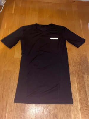 Svart compression tränings-tshirt från A–Z - Svart slimfit träningströja från A–Z med korta ärmar och rund hals. Framtill finns en diskret gul detalj. Materialet är lätt och andas, perfekt för träning eller sport. Snygg och enkel design som funkar till gymmet.