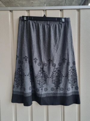 Grå och svart kjol med mönster - Storlek motsvarar M/L. Kjolen är tillverkad i mjukt material med elastisk midja. Köpt på second hand men kom tyvärr inte till användning. Lappen för information om tvätt och material är borttagen av föra ägaren. Vid fler frågor eller bilder är det bara att kontakta mig :)
