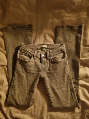 Grå bootcut jeans från ginatricot  - Snygga grå jeans från ginatricot med bootcut-ben och ultra låg midja. Klassisk femficksdesign och coola detaljer på bakfickorna. Jeansen är tillverkade i mjukt jeansmaterial och passar dig som gillar en avslappnad och trendig stil. Paddat mig som vanligtvis är storlek 36. Använd en gång 