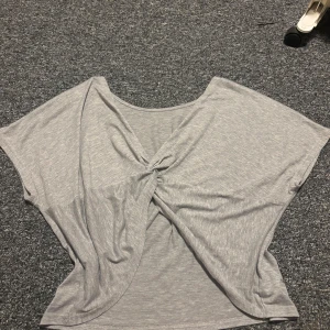 Grå omlottopp - Säljer en ljusgrå omlottopp från SHEIN med snygg twistad detalj framtill. Toppen är ärmlös och har en loose passform som ger en chill vibe. Materialet är mjukt och består av 88% polyester och 12% viskos. Perfekt för dig som gillar enkla men coola plagg.