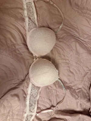 Ljusrosa spets-bh - Säljer en ljusrosa bh med vacker spets längs sidorna. Axelbanden har snygga strassdetaljer som ger extra bling. I storlek C