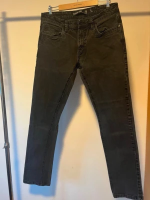 Svarta jeans från Indicode Jeans - Svarta jeans från Indicode Jeans med klassisk femficksdesign och raka ben. Jeansen har en mörk tvätt och tydliga sömmar, samt bälteshällor och knappstängning. Materialet är jeans och passformen är normal, perfekt för dig som gillar stilrena och enkla jeans. Dom är i väldigt bra skick förutom att knappen har fallit av, den finns tyvärr inte kvar och kan inte skickas med men en ny knapp sys enkelt på. 