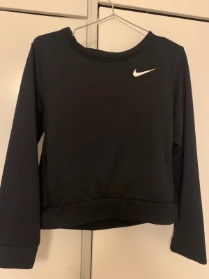 Svart Nike Dri-Fit tröja omlott - Svart långärmad tröja från Nike med Dri-Fit material som andas. Tröjan har en stilren vit Nike-logga på bröstet och en unik omlott-detalj i ryggen. Passformen är normal och tyget är mjukt och skönt, perfekt för träning eller chill. ❤️Tvättar innan jag skickar❤️ 