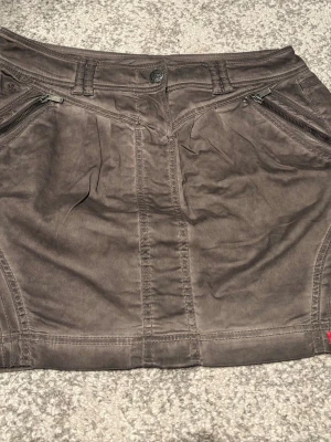 Brun kortkjol från Esprit - Säljer en brun kortkjol från Esprit med snygga detaljer som dragkedjor vid fickorna och markerade sömmar. Kjolen har bälteshällor och knappstängning framtill. Perfekt för dig som gillar en enkel men cool stil.