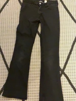 Svarta flare-byxor från H&M - Svarta flare-byxor från H&M med låg midja och justerbar midja. Byxorna har klassisk femficksdesign och är tillverkade i ett mjukt bomullsmaterial med lite stretch. Perfekt för dig som gillar en snygg och trendig siluett.