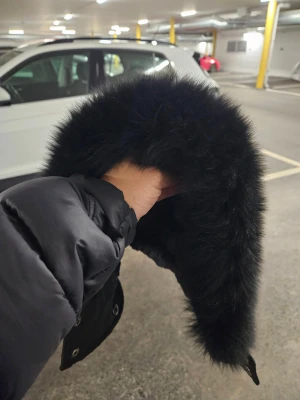 Svart pufferjacka från Moose Knuckles - Säljer en svart  från Knuckles huva med fluffig päls på huvan och snygga silvriga knappar med logotyp. Jackan har en klassisk, stilren look och är perfekt för kalla dagar. Huvan är stor och pälsen är riktigt mjuk och fyllig.