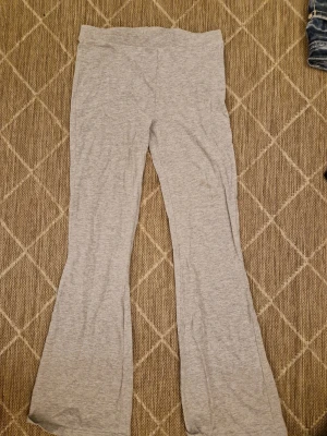 Grå bootcut mjukisbyxor - Säljer ett par grå mjukisbyxor med bootcut-modell. Byxorna är tillverkade i mjukt och stretchigt material, perfekta för en avslappnad stil. De har en enkel design utan synliga detaljer och är riktigt sköna att ha på sig.