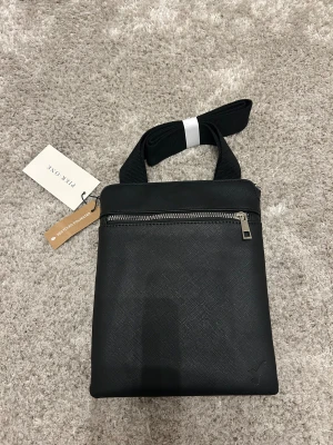 Svart axelväska från Pier One - Snygg svart axelväska från Pier One med två stora fack och dragkedjor i silver. Väskan är tillverkad av återvunnen polyester och har en justerbar axelrem i textil. Perfekt för att bära med sig det viktigaste och har en stilren, minimalistisk look.