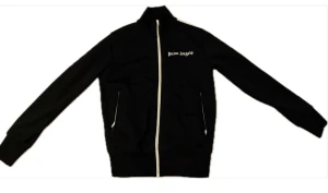 Svart zip tröja från Palm Angels - Svart zip tröja från Palm Angels med vit dragkedja och vita ränder längs ärmarna. Tröjan har hög krage, två fickor med dragkedja och logga på bröstet.