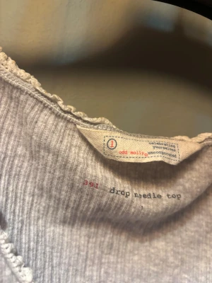 Grå ribbad topp från Odd Molly - Supersöt ljusgrå ribbad topp från Odd Molly med korta ärmar och diskret broderad detalj på ena ärmen. Toppen har en feminin passform med lätt v-ringning och små volangkanter vid hals och ärmslut. Perfekt till jeans eller kjol.💕