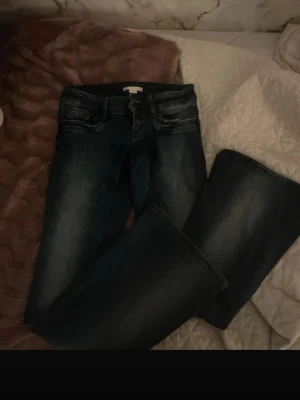 Mörkblå bootcut jeans - Snygga mörkblå jeans med bootcut-modell och lätt slitning på låren. Klassisk femficksdesign och normalhög midja. Perfekta till sneakers eller boots för en cool look.